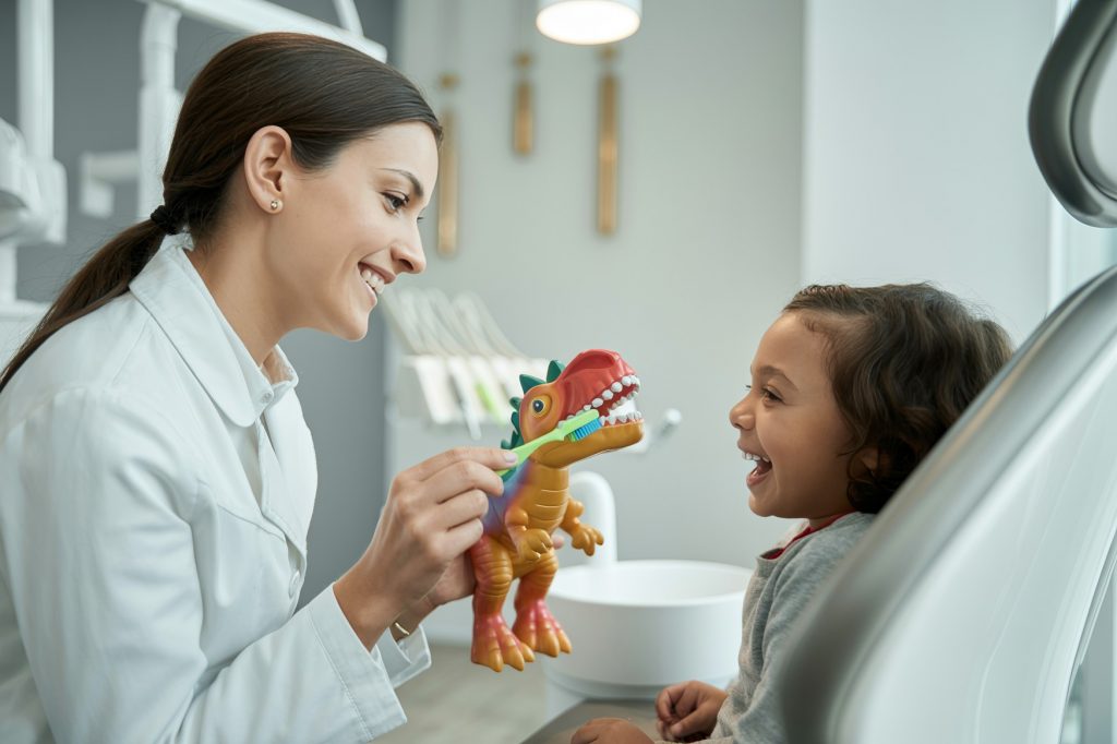A smiling child watches as the dentist places a toothbrush on the dinosaur’s clearly visible teeth.