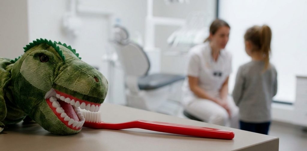"Knuffeldinosaurus met grote tanden op een tandartsbureau met een rode tandenborstel."